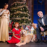 A woman dressed in an elegant gown and a man dressed in a tuxedo look down at a young girl and her dog.