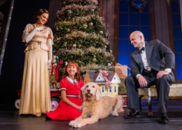 A woman dressed in an elegant gown and a man dressed in a tuxedo look down at a young girl and her dog.