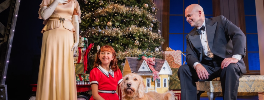 A woman dressed in an elegant gown and a man dressed in a tuxedo look down at a young girl and her dog.