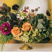 A floral arrangement with greenery, muted yellow tones, and a deep red flower