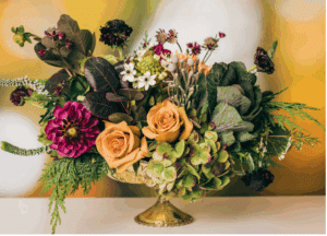 A floral arrangement with greenery, muted yellow tones, and  a deep red flower