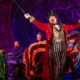 A performer with goatee, red coat, gold vest, and tophat in front of Can-Can dancers at the Moulin Rouge