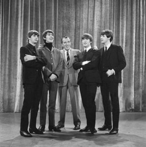 A black and white photograph of The Beatles standing with Ed Sullivan