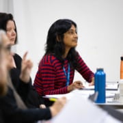 Playwright Vauhini Vara sits at a table with her peers. Papers and drinks are scattered across the table, the team is hard at work.