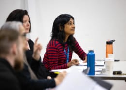 Playwright Vauhini Vara sits at a table with her peers. Papers and drinks are scattered across the table, the team is hard at work.