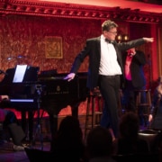 A man strikes a pose onstage, pointing to the audience