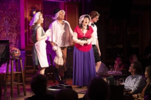 A group of performers sing onstage. They are wearing old-timey costumes and hats thrown on over their regular clothes