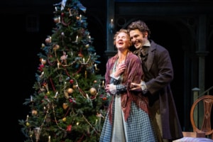 Chloe McLeod and Brian Bohlender. Photo by Jamie Kraus Photography. Belle and her husband stand close together in front of a beautifully decorated Christmas tree with ornaments and garlands. The intimate moment suggests a heartfelt exchange in a warmly lit setting.