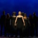Charlotte stands in the center spotlight. The other nine nominees stand in shadow behind her, forming a pyramid.
