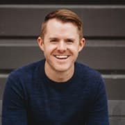 Man in a dark, crewneck shirt with short cropped hair in front of brown siding