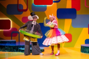 Gerald the Elephant is dressed in swim trunks, a top hat, and an inflatable swim ring on top of his normal clothes. Next to him Piggie is wearing a rainbow tutu, a flower necklace, and green satin gloves on top of her regular clothes.