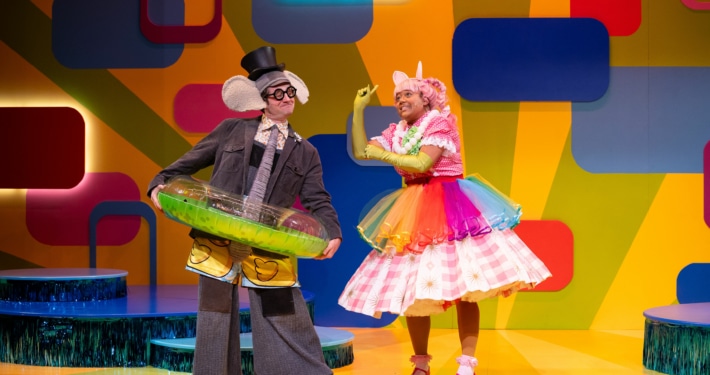 Gerald the elephant and Piggie stand onstage, wearing fun accessories like a pool inner tube, a rainbow tutu, and a top hat.