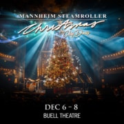 A graphic featuring a glowing, decorated Christmas tree onstage surrounded by instruments and illuminated by dramatic blue and white spotlights.White script reads Mannheim Steamroller Christmas by Chip Davis