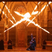 A stage production with bursts of fire filling what appears to be a cathedral