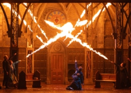 A stage production with bursts of fire filling what appears to be a cathedral