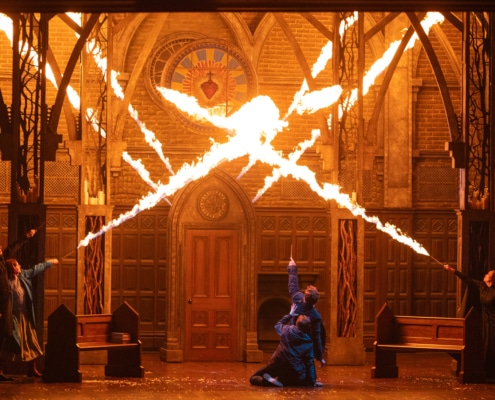 A stage production with bursts of fire filling what appears to be a cathedral