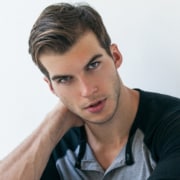Headshot of actor with cropped hair, head angled to side, and black and gray henley shirt.