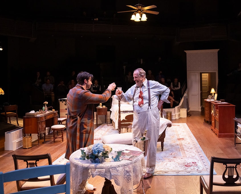 Two men raise glasses in a toast, sharing a moment of camaraderie. The room’s vintage decor and warm lighting add to the celebratory atmosphere.