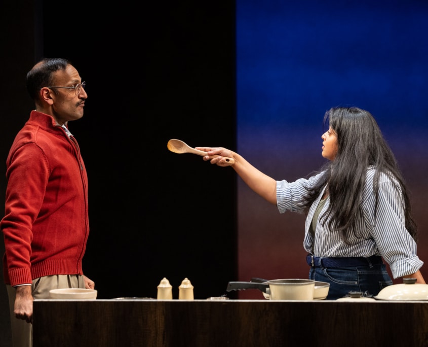 Lakshmi Sen points a wooden spoon at her father, Rajah Sen, in a joking manor while cooking dinner.