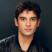 Headshot of an actor on a dark gray background wearing a black shirt with short dark hair.