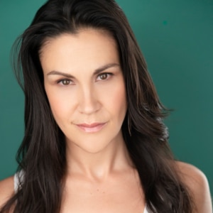 Headshot of an actress in front of a teal background wearing a white tanktop with long straight black hair.
