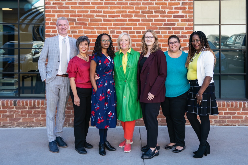 A group of seven people standing in front of a brick wall, posing for a photo.