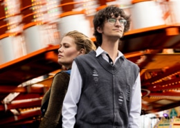 Two people standing in front of a blurred amusement park ride with bright lights and orange structure.