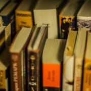 A collection of well-used books of various sizes and colors arranged on a shelf, with some titles visible on the spines.