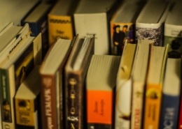 A collection of well-used books of various sizes and colors arranged on a shelf, with some titles visible on the spines.