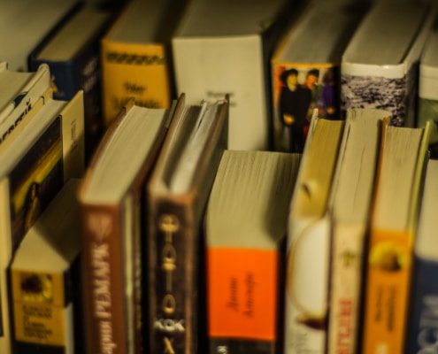 A collection of well-used books of various sizes and colors arranged on a shelf, with some titles visible on the spines.
