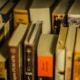 A collection of well-used books of various sizes and colors arranged on a shelf, with some titles visible on the spines.