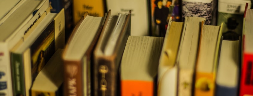 A collection of well-used books of various sizes and colors arranged on a shelf, with some titles visible on the spines.