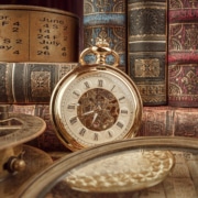Vintage pocket watch with Roman numerals surrounded by antique books, an old calendar, and historical instruments—timeless heritage and history concept.