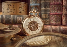 Vintage pocket watch with Roman numerals surrounded by antique books, an old calendar, and historical instruments—timeless heritage and history concept.