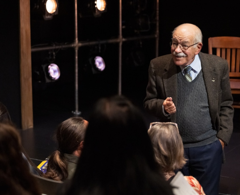 Actor Kenneth Tigar, playing Holocaust survivor Eddie Jaku, stands on a stage as he speaks to an audience.