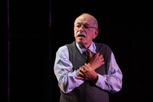 Actor Kenneth Tigar, playing Holocaust survivor Eddie Jaku, puts his hands to his chest while addressing the audience.