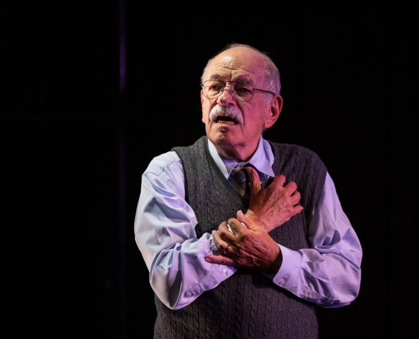 Actor Kenneth Tigar, playing Holocaust survivor Eddie Jaku, puts his hands to his chest while addressing the audience.
