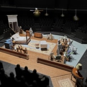 A set model of Cat on a Hot Tin Roof showing a bedroom in a Southern plantation with a bed, vanity, chaise lounge, rug, various chairs, and openings into a hallway and onto a veranda.