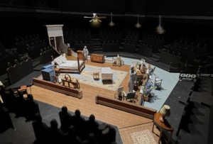 A set model of Cat on a Hot Tin Roof showing a bedroom in a Southern plantation with a bed, vanity, chaise lounge, rug, various chairs, and openings into a hallway and onto a veranda.