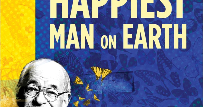 The title treatment in blue spelling "The Happiest Man on Earth" on top of a yellow background with birds and a barb wire fence in the background.