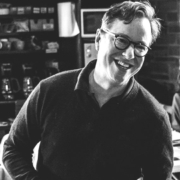 Black and white photo of a man in a dark shirt with glasses who is smiling
