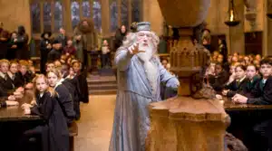 A scene from Harry Potter with Dumbledore standing and gesturing in the Great Hall filled with students."