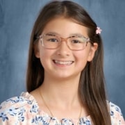Person with long straight brown hair wearing a floral top and a small flower hair clip, posed against a blue-gray studio background.