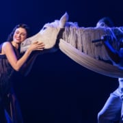 An actress leans in to nuzzle with a large puppet that represents a horse.
