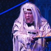 Actress dressed in a white straight jacket with long, white wig holding out a silver tray with appetizers