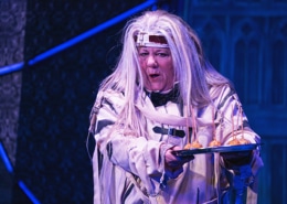 Actress dressed in a white straight jacket with long, white wig holding out a silver tray with appetizers