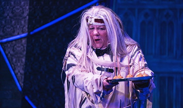 Actress dressed in a white straight jacket with long, white wig holding out a silver tray with appetizers