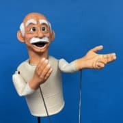 Bright blue background with puppet on rods depicting an old man with white mustache and eyebrows
