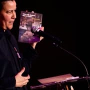 A woman speaking to an audience while holding a book in her hands