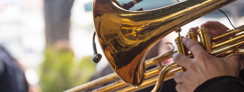 Close up image of a trombone being held by someone in an outdoot setting.